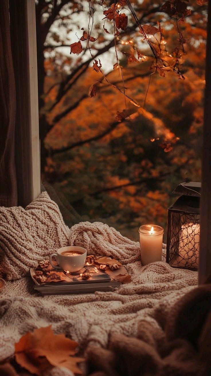 Autumn or fall leaves in the backgroung with a cozy reading nook and candle lit for the perfect fall aesthetics